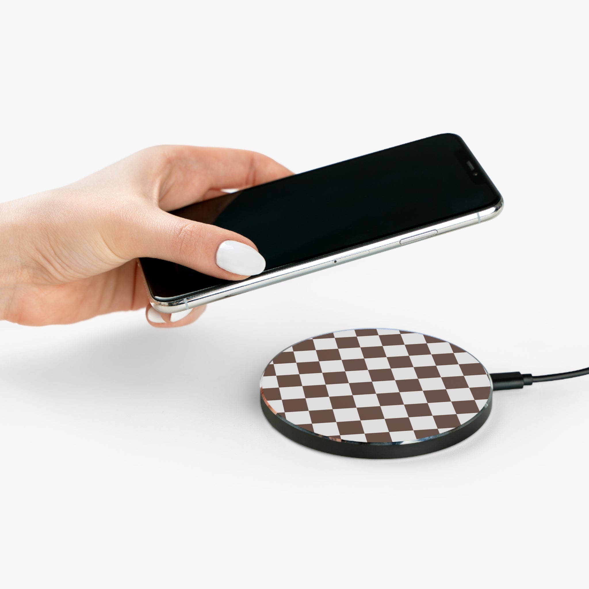 Hand holding a smartphone above a wireless charging pad on a white background